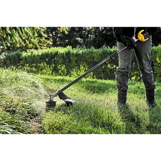 DEWALT DCZ65713X1-XE, DCMAS5713N trimmer in use outdoors, cutting grass in garden. Product for photography category.