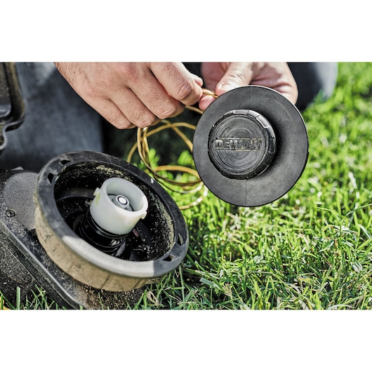 A person replaces string in a DEWALT trimmer head on green grass outdoors.