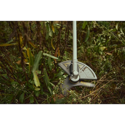DEWALT DCMBC812N-XJ, DCMBC812N grass trimmer head in use outdoors among plants and grass.