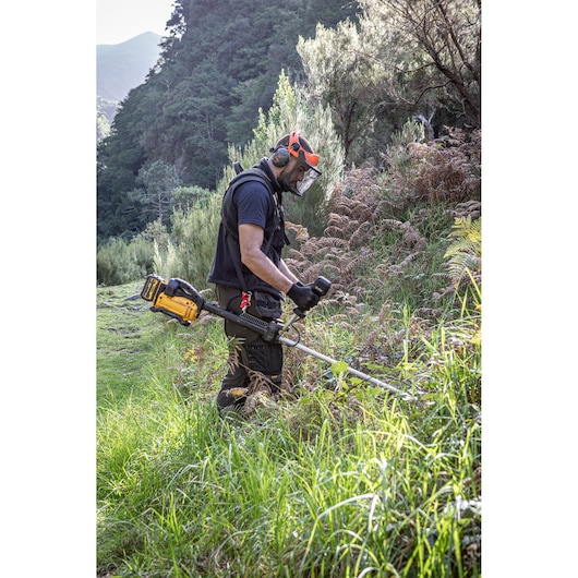 Person uses DEWALT brush cutter DCMBC823N, DCMBC823N-XJ in outdoor area with safety gear.