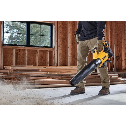 Person cleaning a construction site floor with a yellow DEWALT cordless blower.