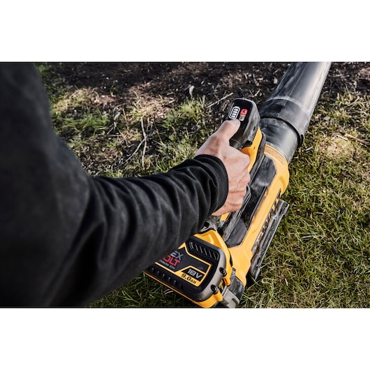 A person using a yellow DEWALT cordless leaf blower outdoors on grass.