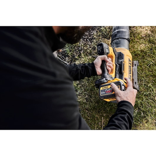 Person holding a DEWALT 54V FLEXVOLT cordless leaf blower outdoors on grass.