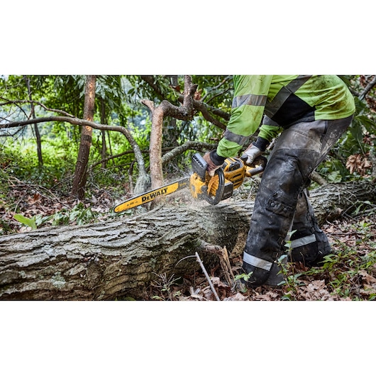 A person using a DEWALT cordless chainsaw to cut a fallen tree trunk outdoors in a forested area.