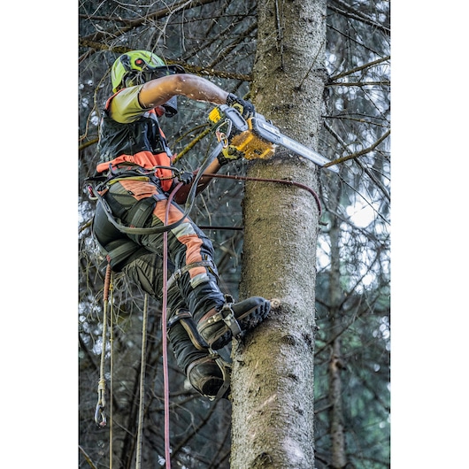 Arborist uses DEWALT chainsaw to cut tree while climbing, wearing safety gear and helmet in a forest setting.