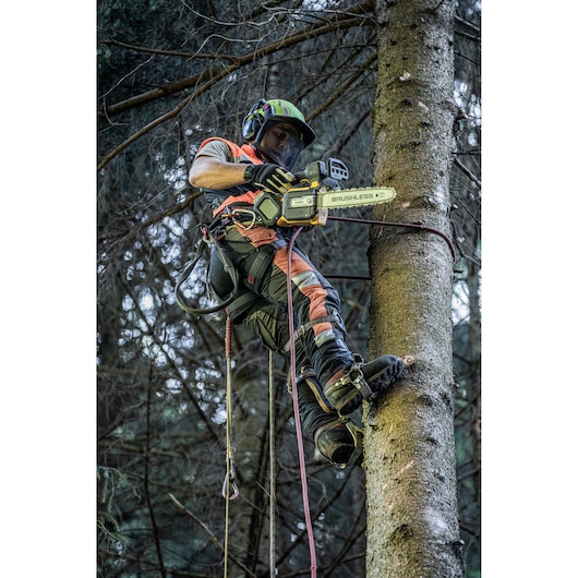 Worker using DEWALT cordless chainsaw, climbing tree with safety gear in a forest.
