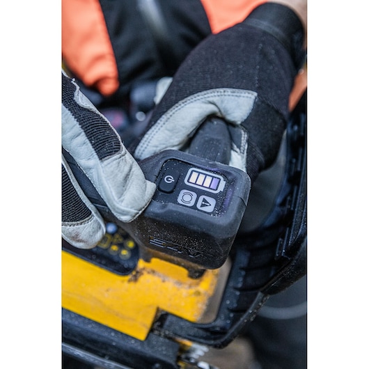 A gloved hand presses controls on a DEWALT tool, focusing on its digital power and battery indicator panel.