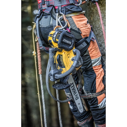 DEWALT cordless chainsaw attached to a worker’s harness during tree climbing in safety gear.