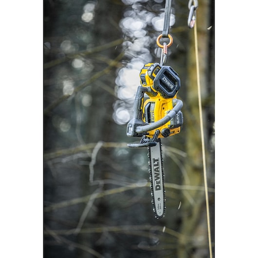 DEWALT cordless chainsaw hanging from a rope in a forest setting.