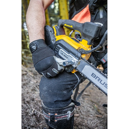 Gloved hand holding a DEWALT cordless chainsaw outdoors, adjusting chain tension.