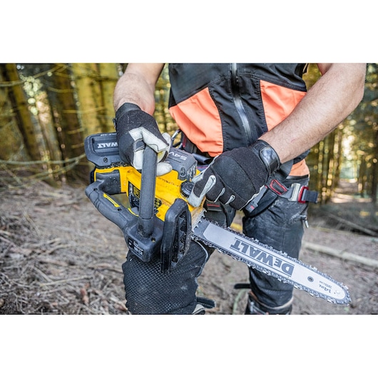Person wearing gloves uses a DEWALT battery-powered chainsaw outdoors in a forest.