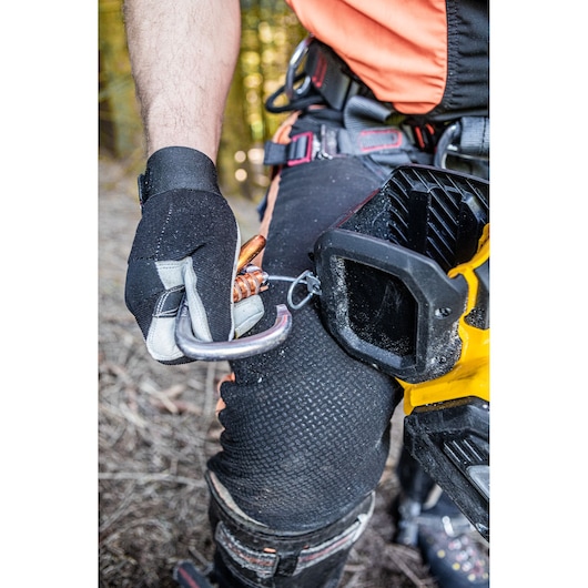 Gloved hand clips carabiner to DEWALT tool on worker’s belt. Outdoor setting, safety gear visible.