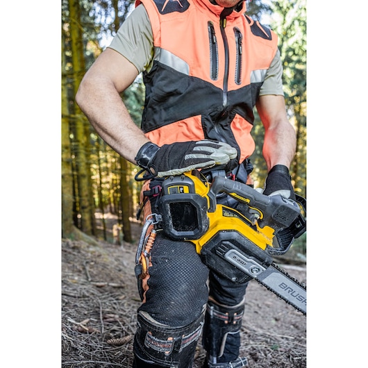 Person in safety gear holding a DEWALT chainsaw in a forest. Only lower body and tool are visible.