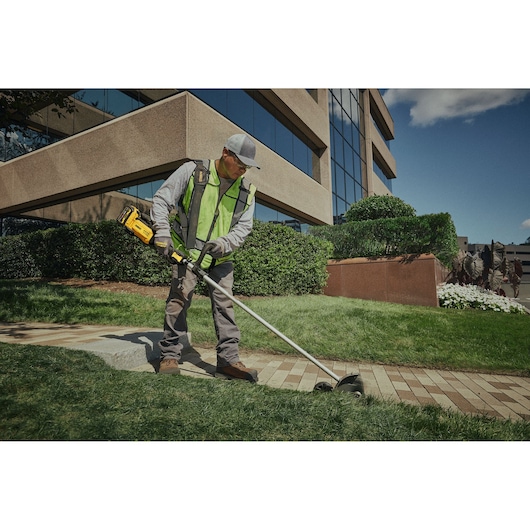 Person using a DEWALT cordless edger to trim grass along a walkway in front of an office building.