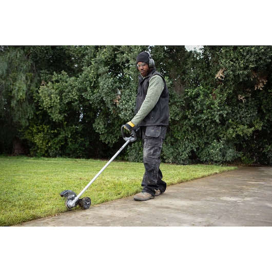 Person uses a DEWALT edger to trim grass along a walkway, with trees in the background.