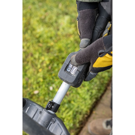 Gloved hand adjusting DEWALT garden tool control near grass, showing detailed buttons and battery indicator.