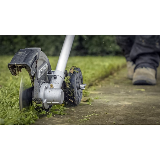 DEWALT lawn edger trimming grass along a walkway with user in boots in the background.