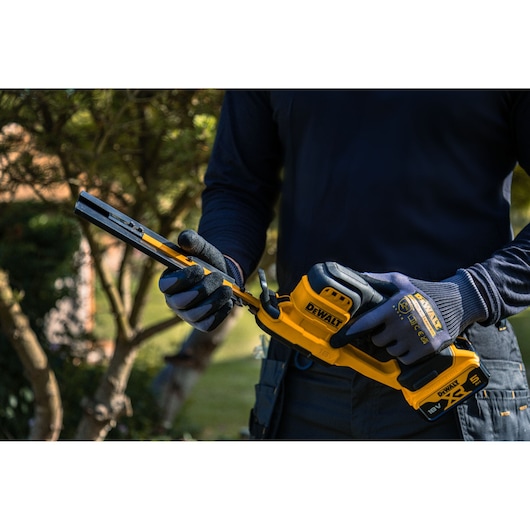 Person holds DEWALT tool in garden. SKUs: DCMHT520N-XJ, DCMHT520D1-QW, DCMHT520D1, DCMHT520N.
