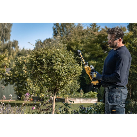 Person using DEWALT hedge trimmer models DCMHT520N-XJ, DCMHT520D1-QW, DCMHT520D1, DCMHT520N outdoors.