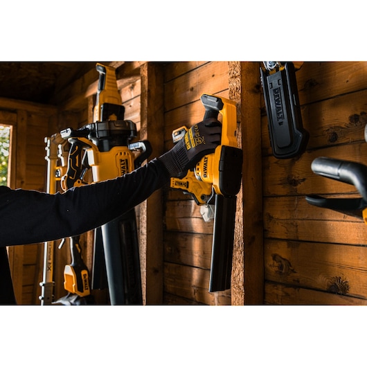 DEWALT tools on wall, gloved hand holds DCMHT520N-XJ, DCMHT520D1-QW, DCMHT520D1, DCMHT520N. Wooden shed interior.