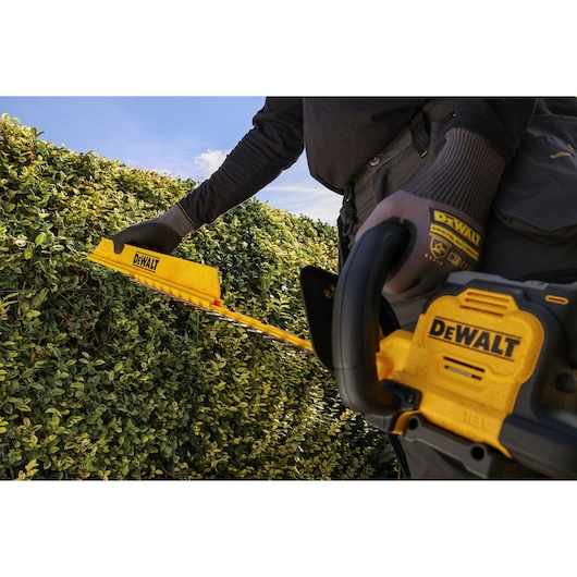 DEWALT hedge trimmer in use outdoors. SKUs: DCMHT567N, DCMHT567P1-QW, DCMHT567N-XJ, DCMHT567P1.