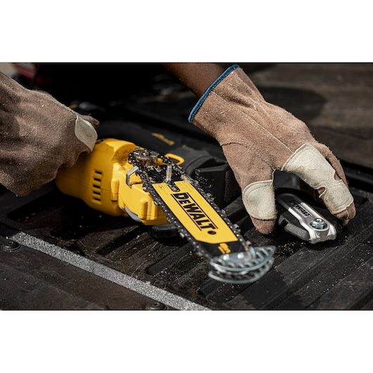 Worker with gloves assembling or inspecting a yellow DEWALT chainsaw and tool on a black surface.