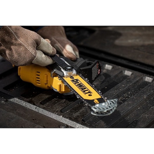 Gloved hands adjust the chain on a yellow DEWALT DCMPS520N pole saw, lying on a black textured surface.