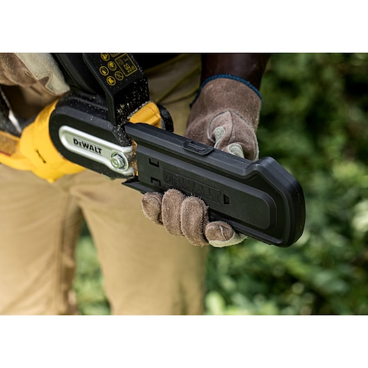 Gloved hand holds DEWALT chainsaw with protective cover outdoors. Tool and cover are branded DEWALT.