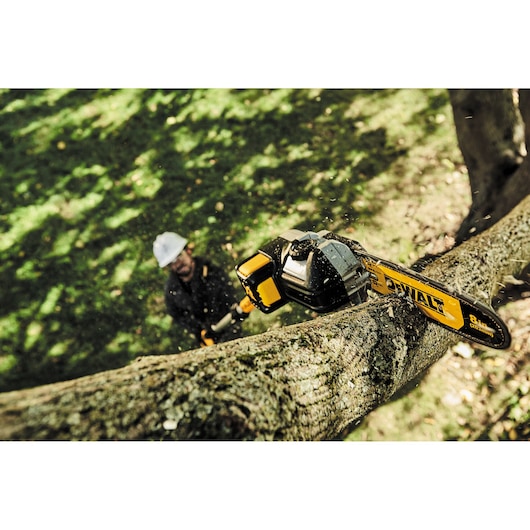 DEWALT pole saw cutting a tree branch outdoors with operator blurred in the background.