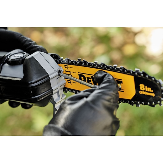 Person adjusts DEWALT 8-inch chain saw blade outdoors with a screwdriver, wearing black gloves.