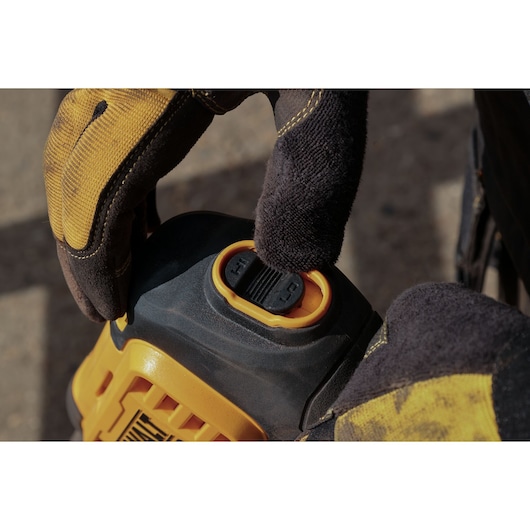 Close-up of DEWALT DCMPW1000N, DCMPW1000N-XJ control button used by a gloved hand outdoors.