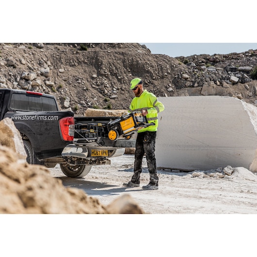 Worker unloads DEWALT power tool from truck at a quarry. Dusty environment with stone blocks and rocky background.