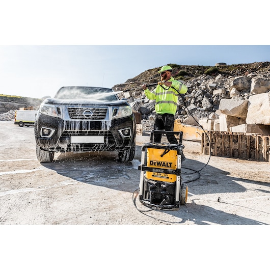 DEWALT pressure washer being used to clean a black pickup truck outdoors at a construction site.