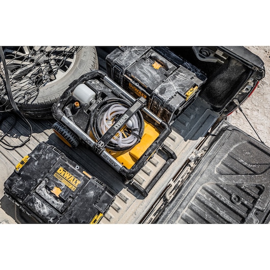 DEWALT DCMPW1600 power washer and tool boxes are shown in a dusty truck bed for worksite use.