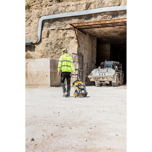 Person pulls a DEWALT DCMPW1600 pressure washer near a construction tunnel and loader.