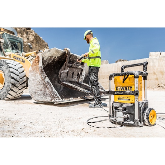 DEWALT pressure washer cleaning construction vehicle bucket outdoors at a worksite.