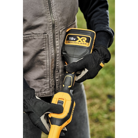 Person wearing gloves holds a DEWALT 18V XR Brushless tool outdoors, focusing on the handle and battery.