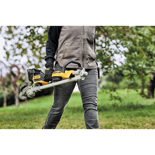 Person holding a DEWALT cordless string trimmer outdoors in a grassy area.