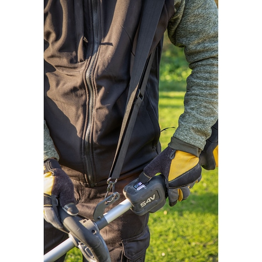 Person wearing gloves and holding a DEWALT 54V garden tool outdoors, dressed in a zippered jacket.
