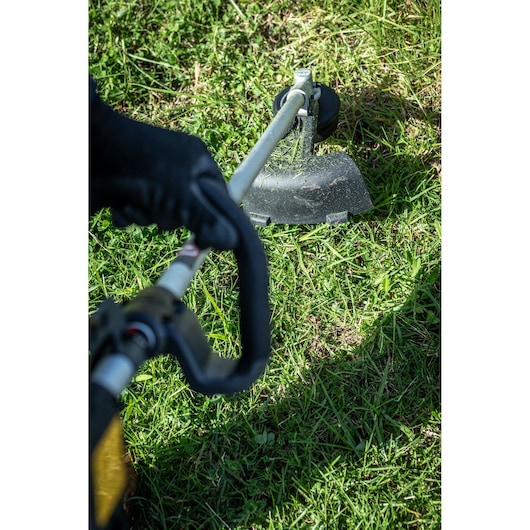 DEWALT grass trimmer DCMST911N and DCMST911N-XJ in use on lawn, close-up view of handle and cutting head.