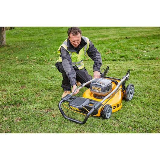 Person with safety vest adjusting DEWALT lawn mower DCMW564N on grass.