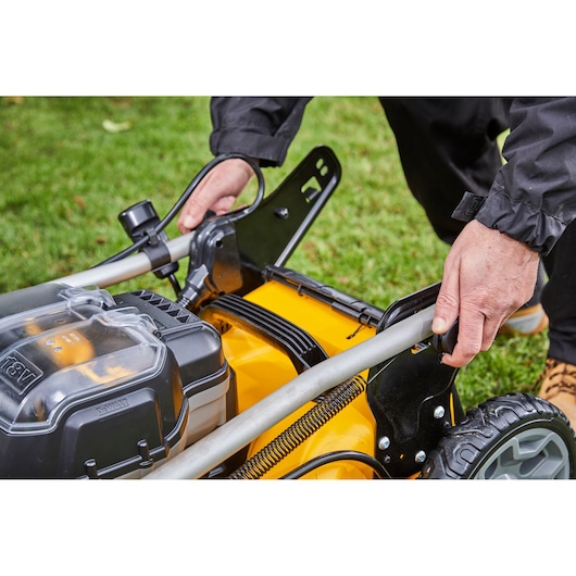 Hands adjusting the handle of a yellow DEWALT lawn mower on grass.