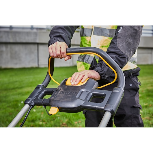 Person operating a DEWALT lawn mower, focusing on the handle and control panel outdoors.