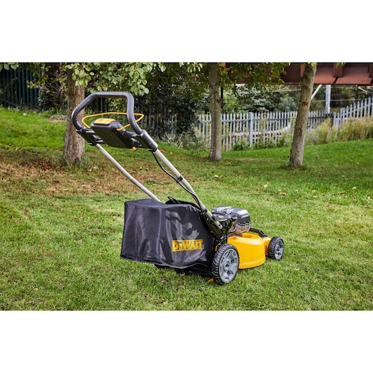 DEWALT cordless lawn mower on grass with trees and fence in background.