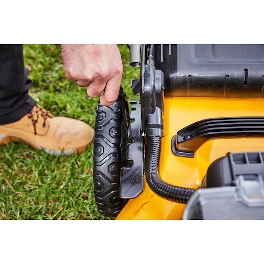 Hand adjusting the wheel height on a yellow DEWALT lawn mower, close-up view outdoors on grass.