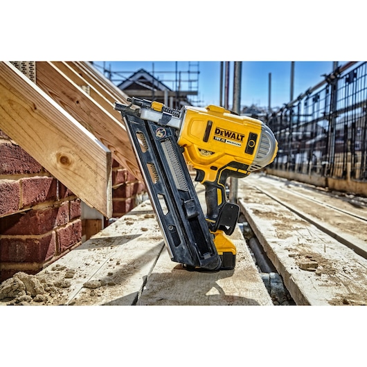 DEWALT DCN692P2 nail gun placed on wood at a construction site, shown in bright daylight.