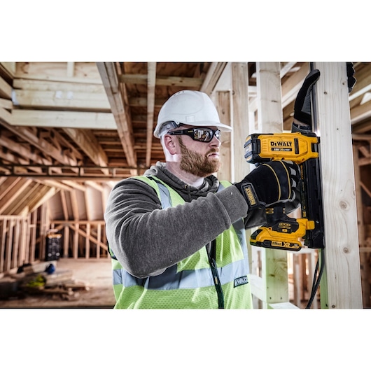 Worker uses a DEWALT DCN701D2 tool to fix a wire to wooden framing at a construction site.