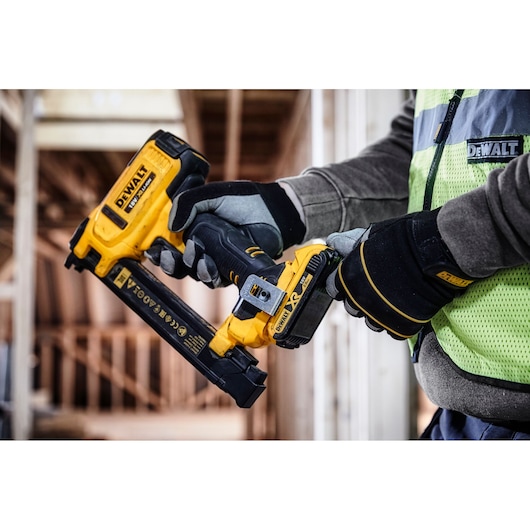 Gloved hands hold a DEWALT DCN701D2 cordless tool at a construction site.