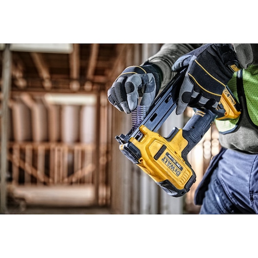 Worker loads nails into a yellow DEWALT cordless nailer on a construction site.