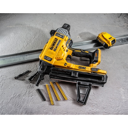 DEWALT DCN890P2 battery nailer with accessories and fasteners on a concrete surface.